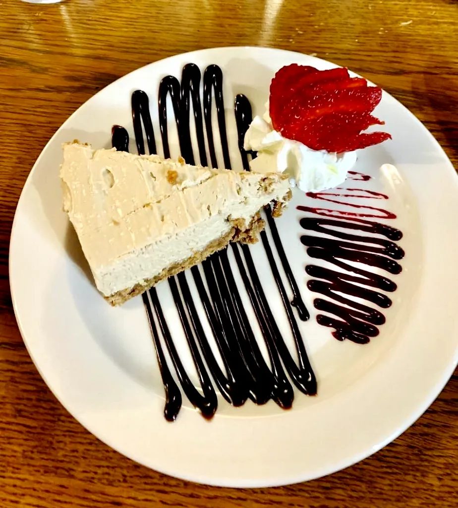 A slice of homemade cheesecake with cream and chocolate sauce